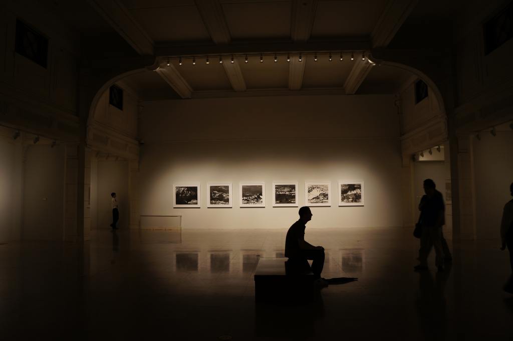 Il s'agit d'une photo libre de droit dans une salle d'un musée. L'ambiance est sombre. Un usager est assis sur un banc   .
